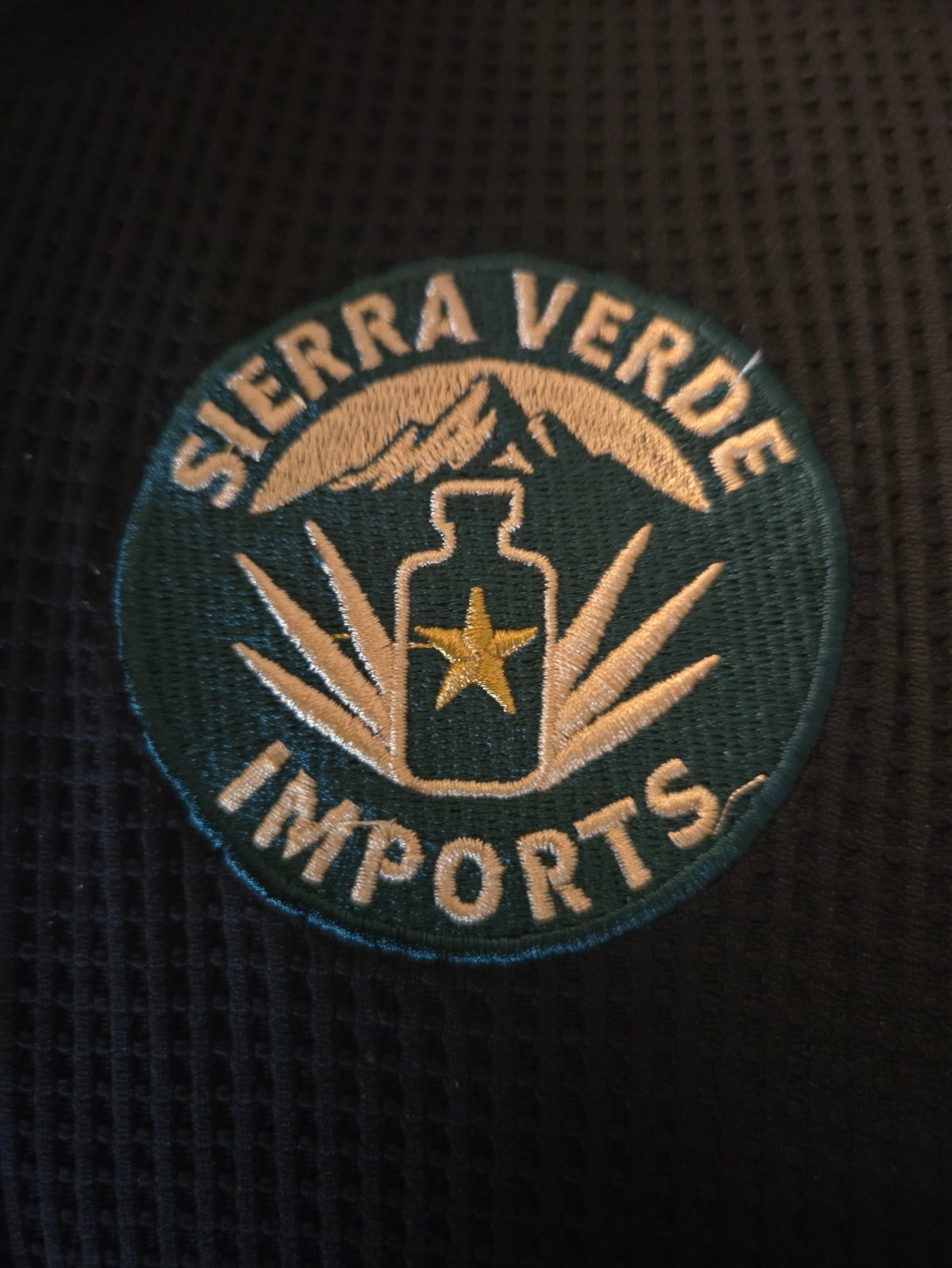 Sierra Verde Imports circular embroidered logo patch with bottle and star design on dark fabric